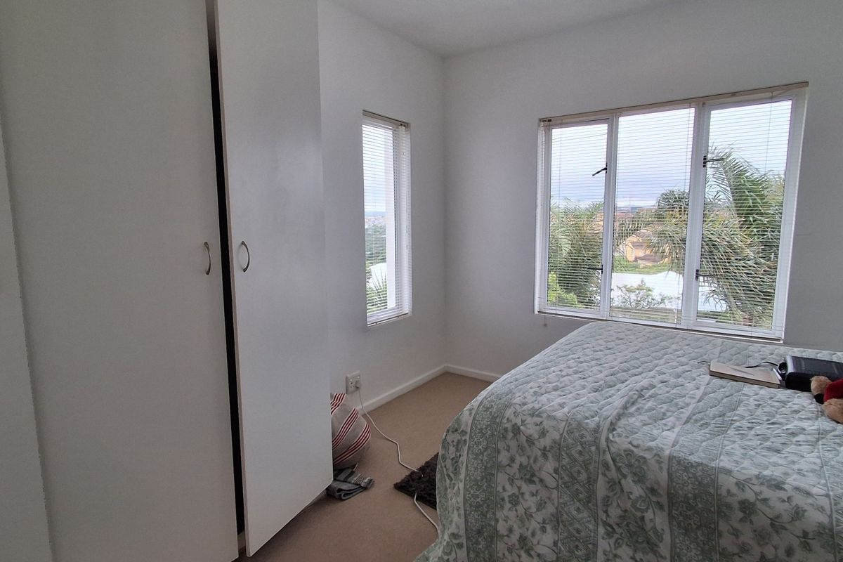 A bright bedroom featuring built-in cupboards, carpeted flooring, and large windows providing natural light and exterior views.