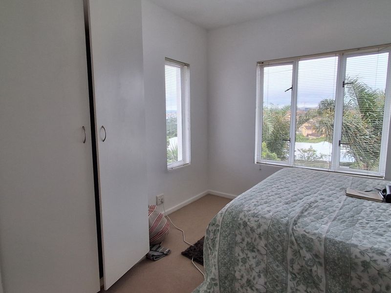 A bright bedroom featuring built-in cupboards, carpeted flooring, and large windows providing natural light and exterior views.