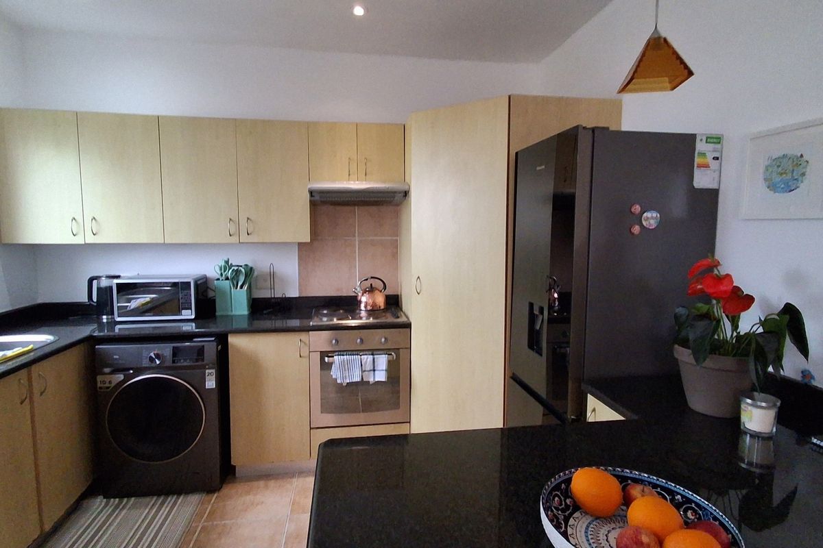 A functional kitchen featuring light wood cabinetry, dark granite countertops, integrated oven and hob, and a tiled backsplash with ample storage space.
