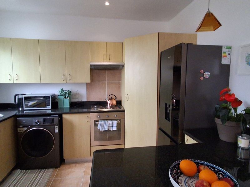 A functional kitchen featuring light wood cabinetry, dark granite countertops, integrated oven and hob, and a tiled backsplash with ample storage space.