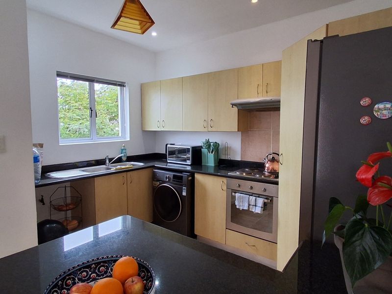 A functional kitchen featuring light wood cabinetry, dark countertops, a built-in oven with hob, and an integrated extractor fan.