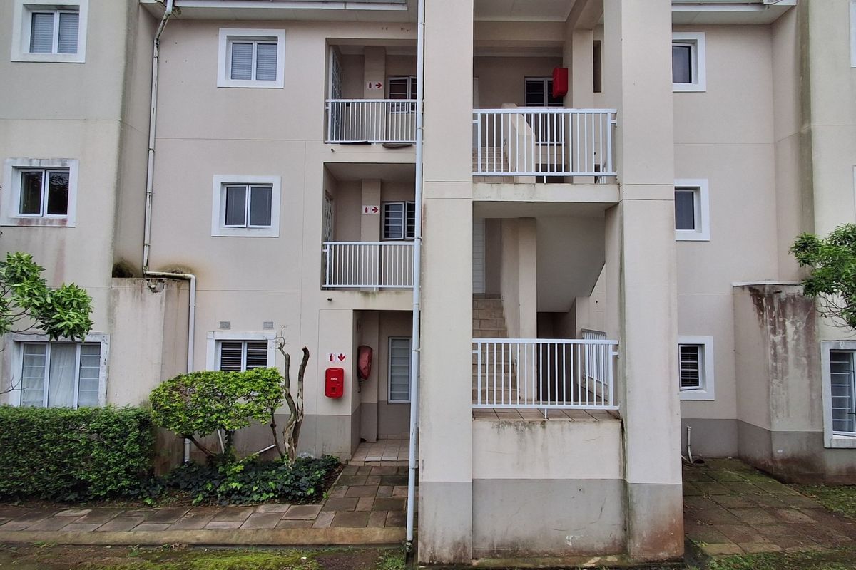 Rear elevation of an apartment building featuring multi-level balconies, external staircases, and paved ground-level walkways.