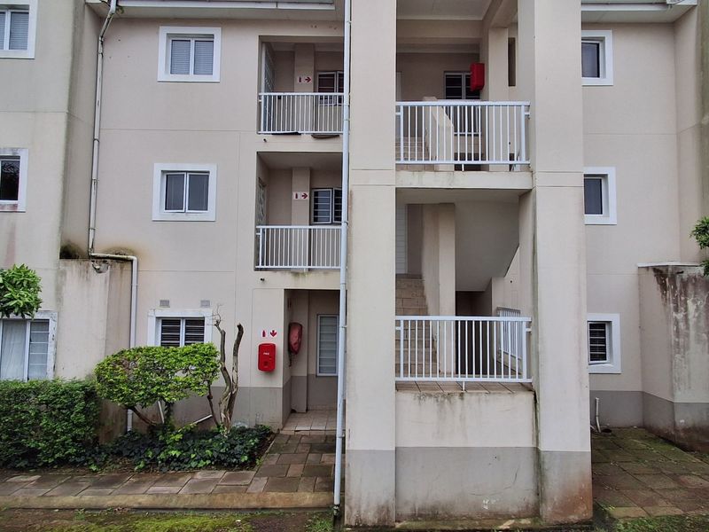 Rear elevation of an apartment building featuring multi-level balconies, external staircases, and paved ground-level walkways.
