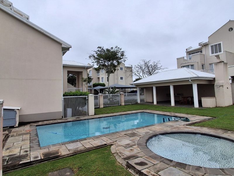 Communal outdoor area featuring a swimming pool, spa, stone paved surround, and a covered patio space within an apartment complex.