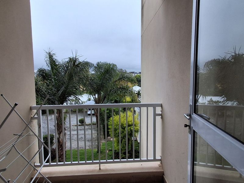 A private balcony featuring a metal balustrade and a glass sliding door, offering an elevated view of the surrounding greenery and parking area.