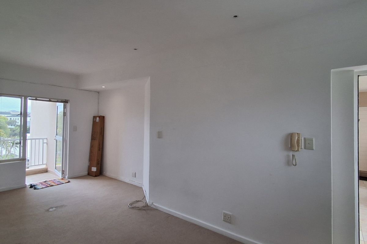 An empty living room featuring neutral carpet, recessed lighting, an intercom system, and direct access to a private balcony through a sliding glass door.