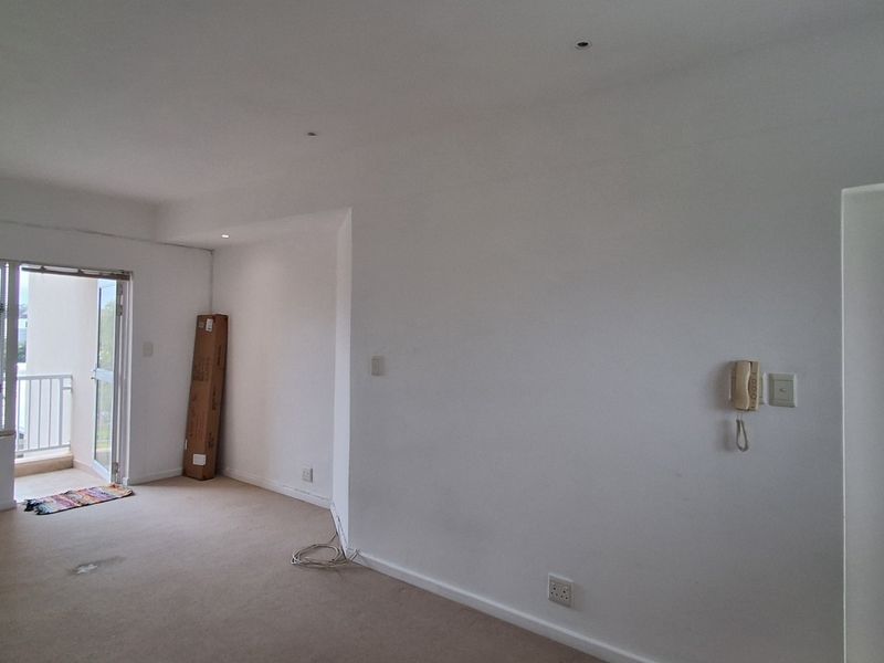 An empty living room featuring neutral carpet, recessed lighting, an intercom system, and direct access to a private balcony through a sliding glass door.