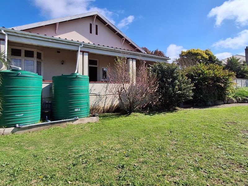 Rear view of the house featuring a covered patio, established garden, and dual green water storage tanks connected to the gutter system.
