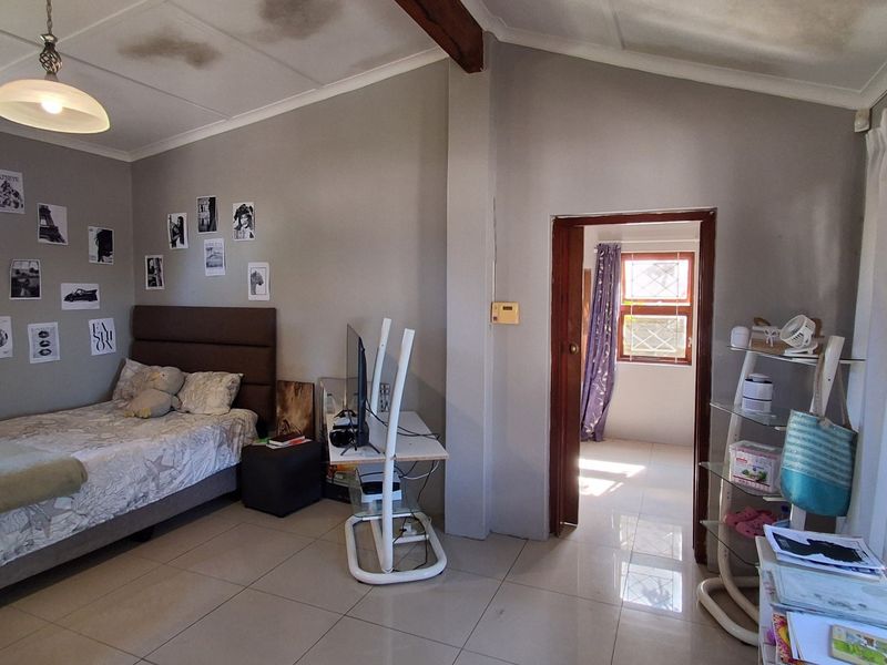A bedroom featuring tiled flooring, a vaulted ceiling with exposed timber beam, and aluminium window frames, showing signs of ceiling water damage.