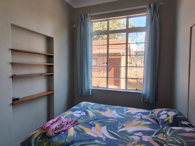 A bedroom featuring built-in wall shelving and a window with security bars, providing natural light and functional storage space.