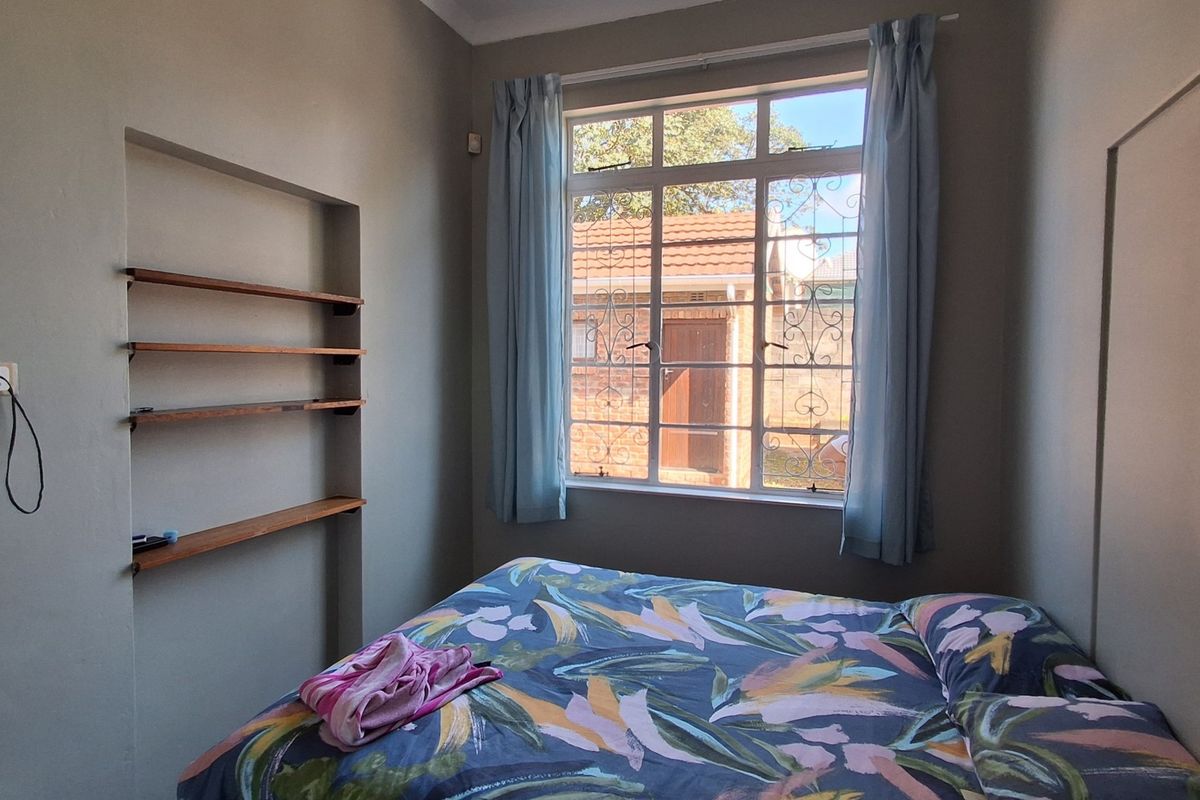 A bedroom featuring built-in wall shelving and a window with security bars, providing natural light and functional storage space.