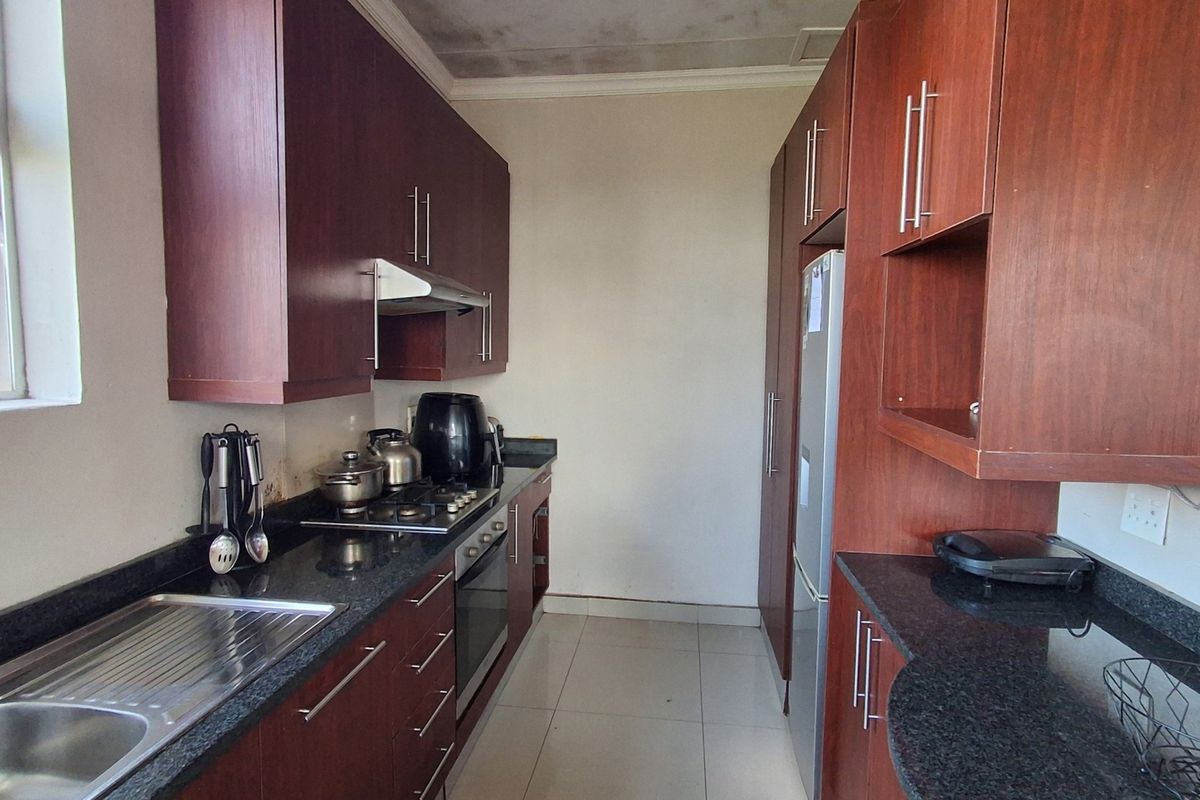 A galley-style kitchen featuring dark wood cabinetry, granite countertops, and built-in appliances, with visible ceiling water staining requiring attention.