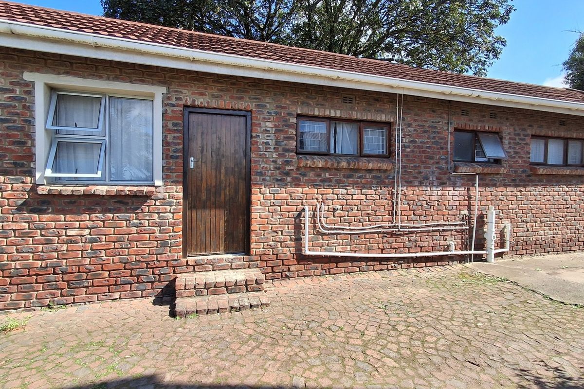 Rear exterior view of the property featuring a face brick facade, tiled roof, and paved courtyard area with accessible entry door.