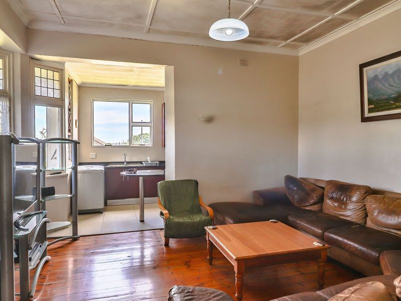 Open plan living area featuring original timber flooring, a bay window, and a connected kitchen space with built-in cabinetry and sink.