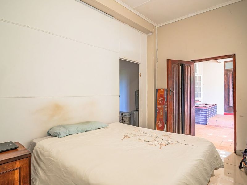 A bedroom featuring tiled flooring and a timber door leading to an outdoor patio area, with visible staining on the wall paneling.