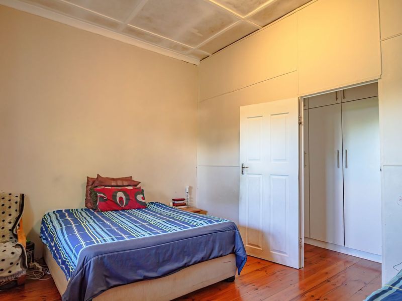 Bedroom featuring timber flooring, built-in cupboards, and a panelled ceiling. The space requires cosmetic updates to improve its overall condition.