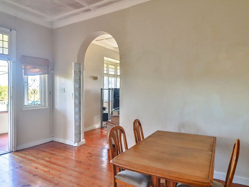 Dining area featuring original hardwood flooring, a classic archway, and a leaded glass window with access to an outdoor balcony.