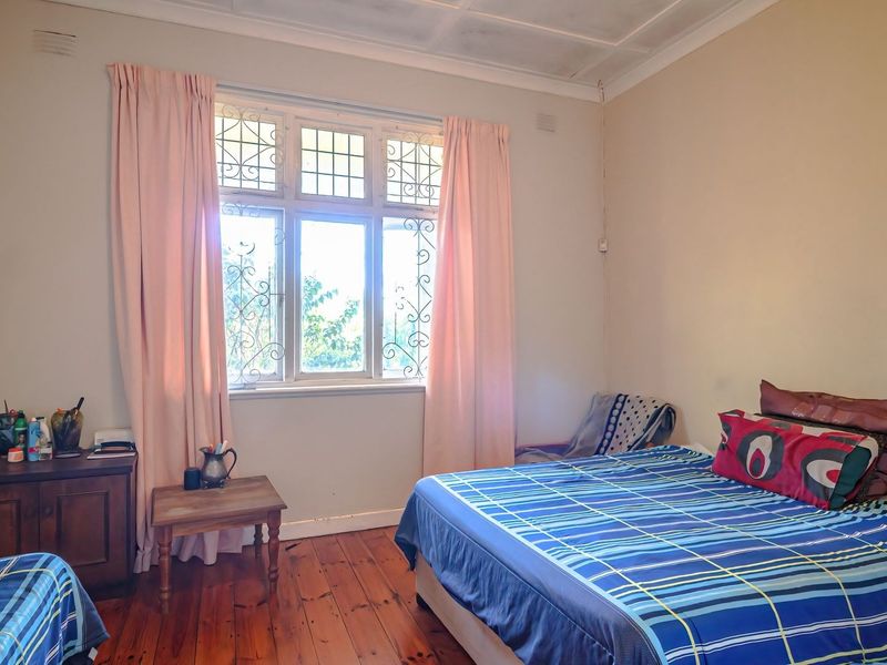 A bedroom featuring original timber flooring, security bars on the window, and built-in storage, offering a classic layout with potential for cosmetic updates.