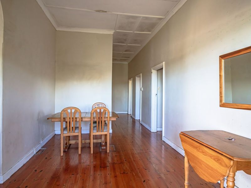 A spacious hallway featuring original timber flooring and multiple access points to adjoining rooms, with potential for cosmetic updates to the ceiling and walls.