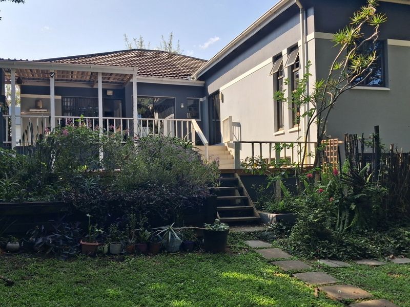 Rear view of the property featuring a raised timber deck, covered patio area, and a landscaped garden with a stone pathway.
