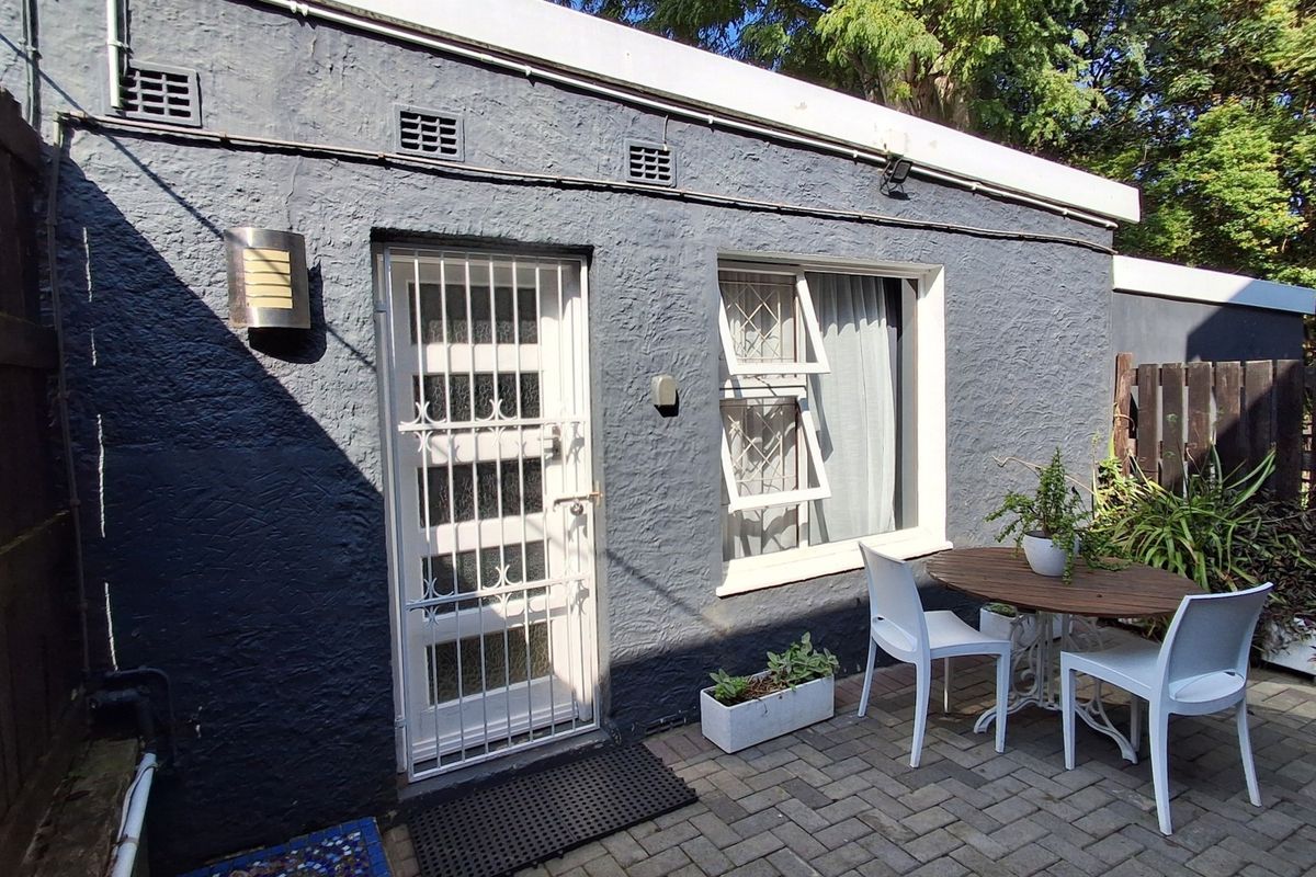 Rear exterior view of the property featuring a paved patio area, security gate, and top-hung window set against a dark textured wall.
