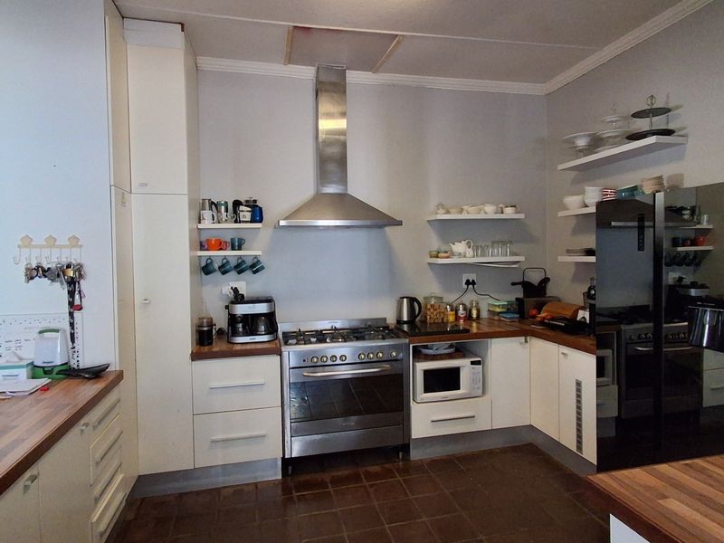 A functional kitchen featuring wooden countertops, a stainless steel gas stove with extractor fan, built-in cabinetry, and open shelving for storage.