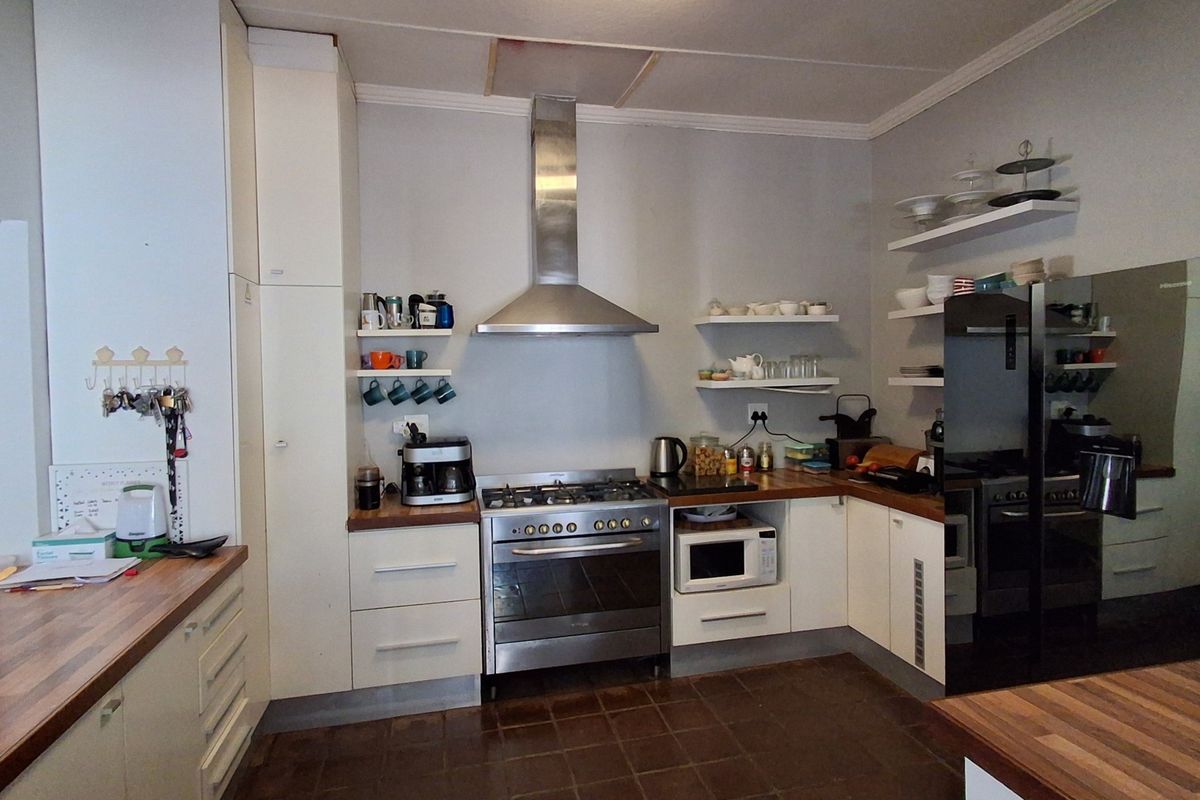 A functional kitchen featuring wooden countertops, a stainless steel gas stove with extractor fan, built-in cabinetry, and open shelving for storage.
