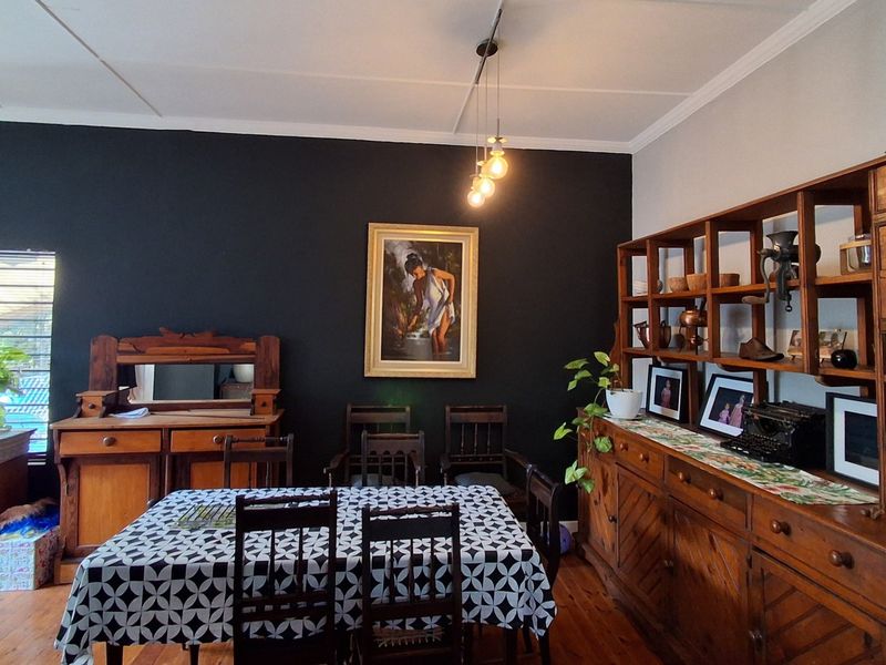 A dining room featuring hardwood flooring, crown molding, and a dark accent wall, illuminated by track and pendant lighting.
