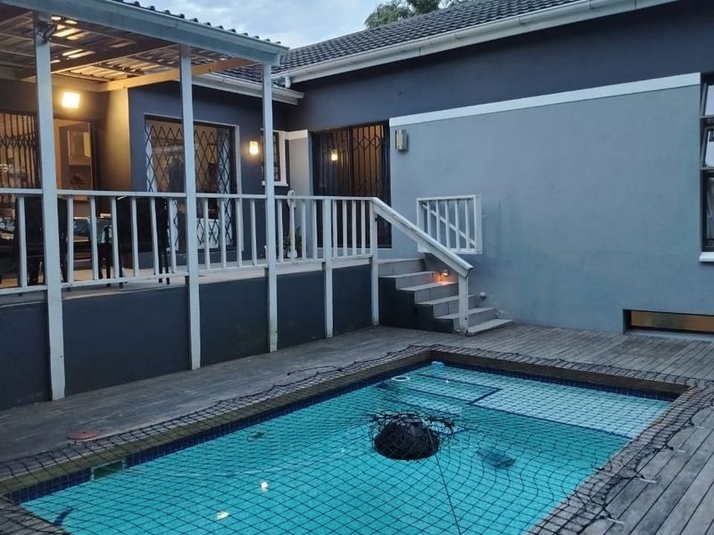 Outdoor pool area featuring timber decking, a covered patio with railing, and a safety net, providing a functional space for relaxation and entertainment.