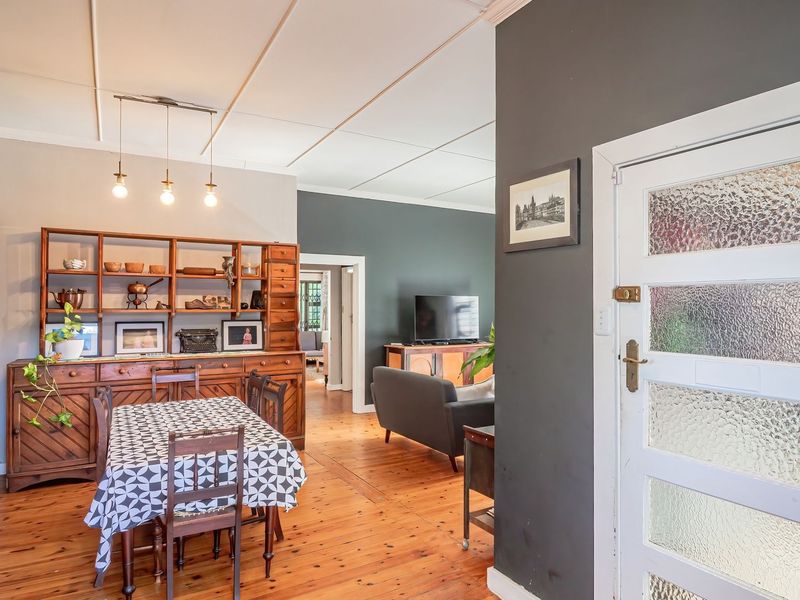 Open-plan living and dining area featuring warm timber flooring, coved ceilings, and a characterful textured glass panel door.