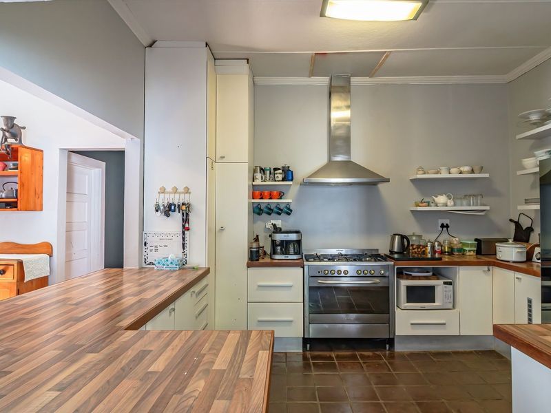 A functional kitchen featuring wooden countertops, stainless steel gas stove with extractor fan, built-in cabinetry, and open shelving.
