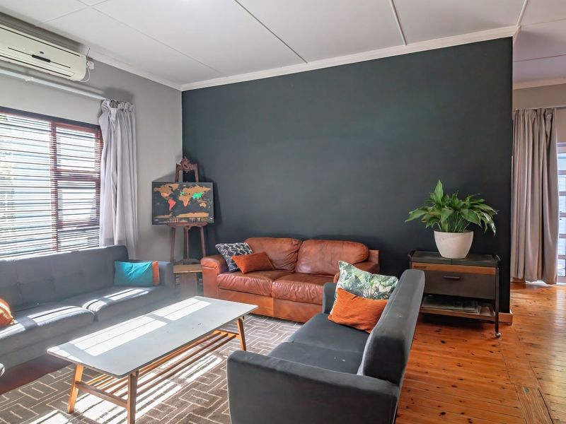 A living room featuring polished timber flooring, a split-system air conditioner, and natural light through venetian blinds, leading to an outdoor area.
