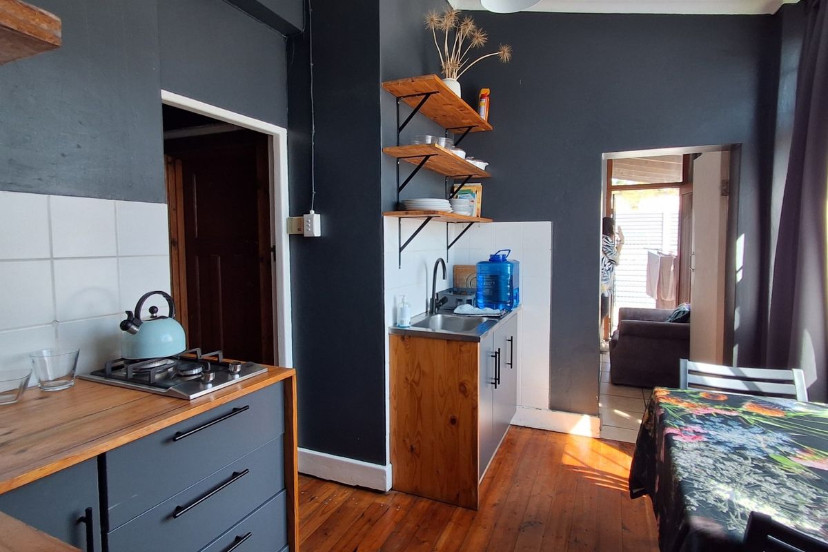 A compact kitchen featuring dark cabinetry, wooden countertops, a gas hob, and a stainless steel sink with open shelving against a dark feature wall.