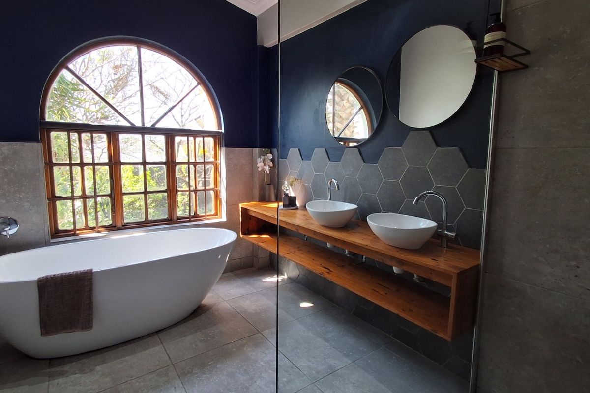 Modern bathroom featuring a freestanding bathtub, double vessel sinks on a timber vanity, and stylish hexagonal wall tiling under an arched window.