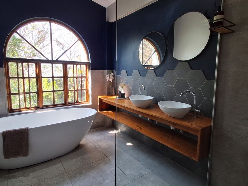Modern bathroom featuring a freestanding bathtub, double vessel sinks on a timber vanity, and stylish hexagonal wall tiling under an arched window.