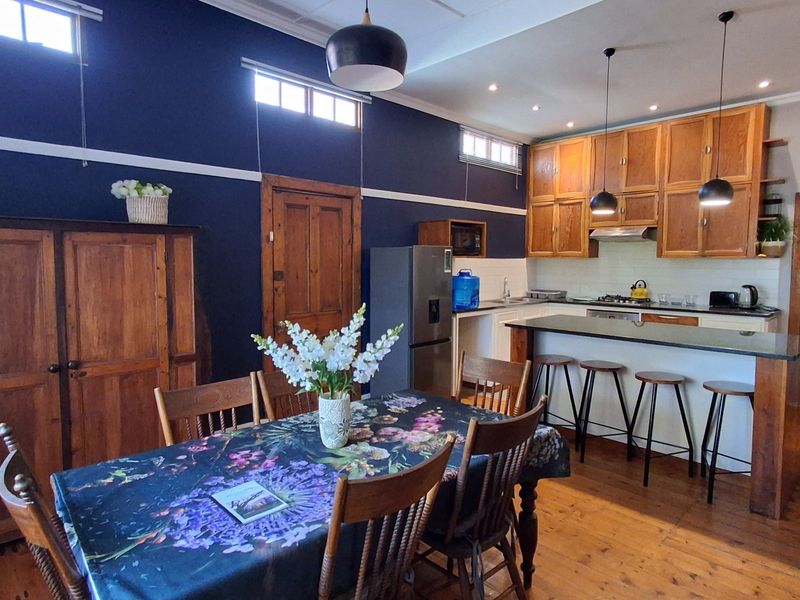Open plan kitchen and dining area featuring wooden cabinetry, stone breakfast bar, hardwood flooring, and high ceilings with transom windows.
