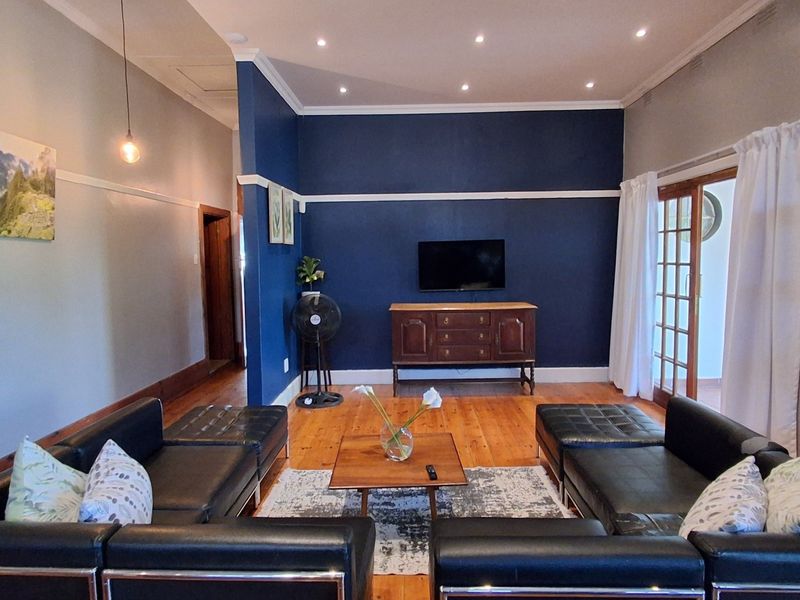 A spacious living room featuring polished hardwood flooring, a bold navy accent wall, recessed lighting, and classic french doors leading to an outdoor area.