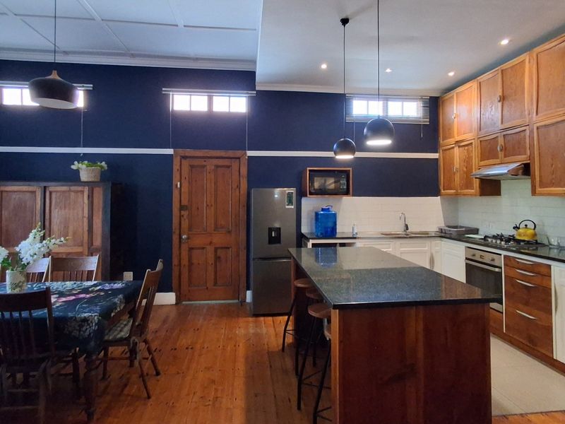 Spacious open-plan kitchen and dining area featuring timber cabinetry, granite countertops, a central island, and warm timber flooring with high ceilings.