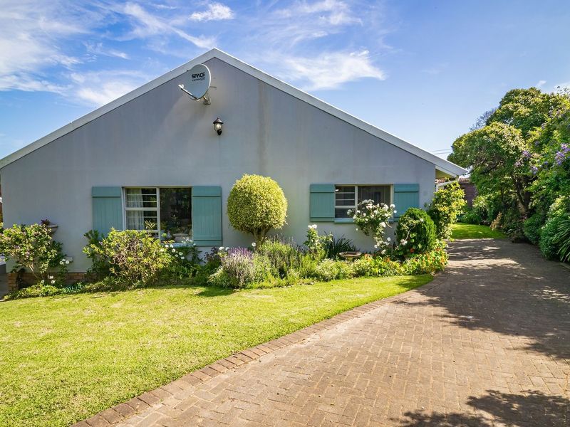 A well-maintained front exterior view of the house featuring a paved driveway, landscaped garden, and classic window shutters.