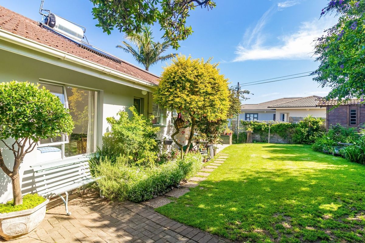 A well-maintained rear garden featuring a paved patio area, lush lawn, and established landscaping, with a solar water heater visible on the roof.