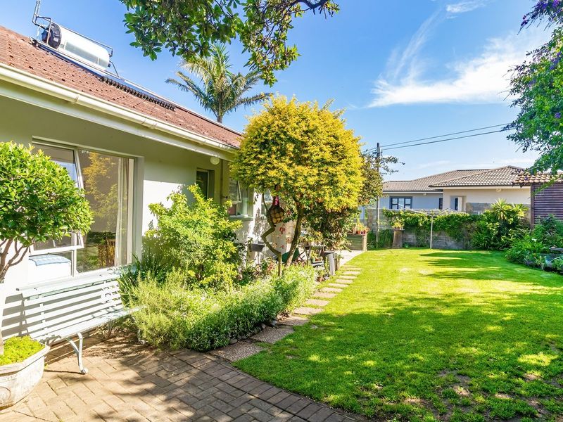 A well-maintained rear garden featuring a paved patio area, lush lawn, and established landscaping, with a solar water heater visible on the roof.