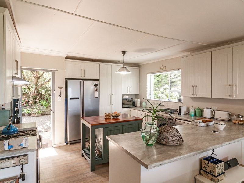 A bright, functional kitchen featuring white cabinetry, stone-look laminate countertops, a central island, and direct access to the rear garden area.