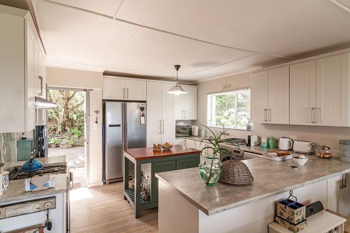 A bright, functional kitchen featuring white cabinetry, stone-look laminate countertops, a central island, and direct access to the rear garden area.
