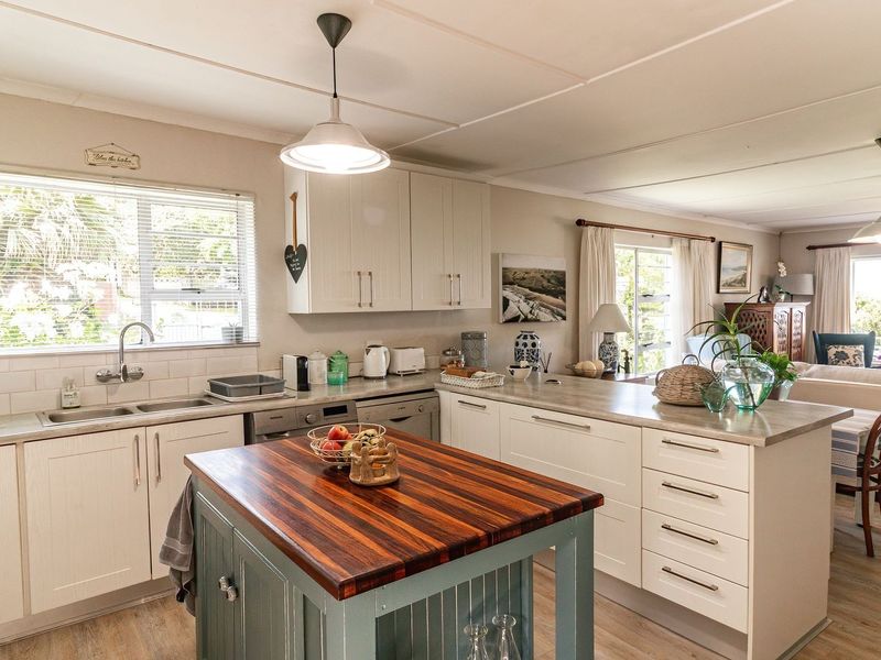 Bright open-plan kitchen and living area featuring a central island, modern cabinetry, double sink, and light-toned laminate flooring throughout.