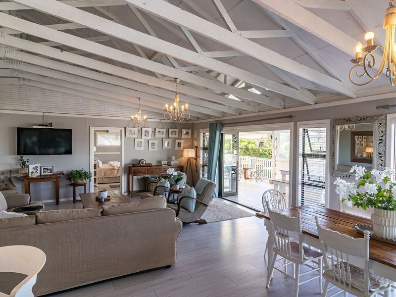 Spacious open-plan living and dining area featuring vaulted ceilings with exposed white timber trusses, laminate flooring, and large sliding doors leading to the patio.