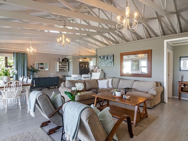 Spacious open-plan living and dining area featuring high vaulted ceilings with exposed timber trusses, light laminate flooring, and neutral wall finishes.