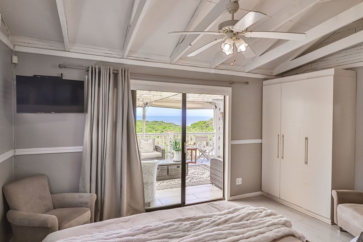 A bright bedroom featuring exposed beam ceilings, a ceiling fan, built-in wardrobes, and sliding glass doors opening onto a private balcony with scenic views.