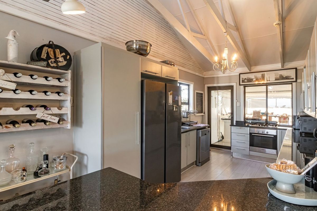 A well-appointed kitchen featuring granite countertops, built-in cabinetry, integrated appliances, and a vaulted ceiling with exposed timber beams, offering a bright and functional space.
