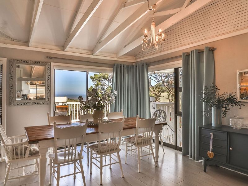 Bright dining room featuring a vaulted ceiling with exposed beams, laminate flooring, and large sliding glass doors that open to an outdoor view.