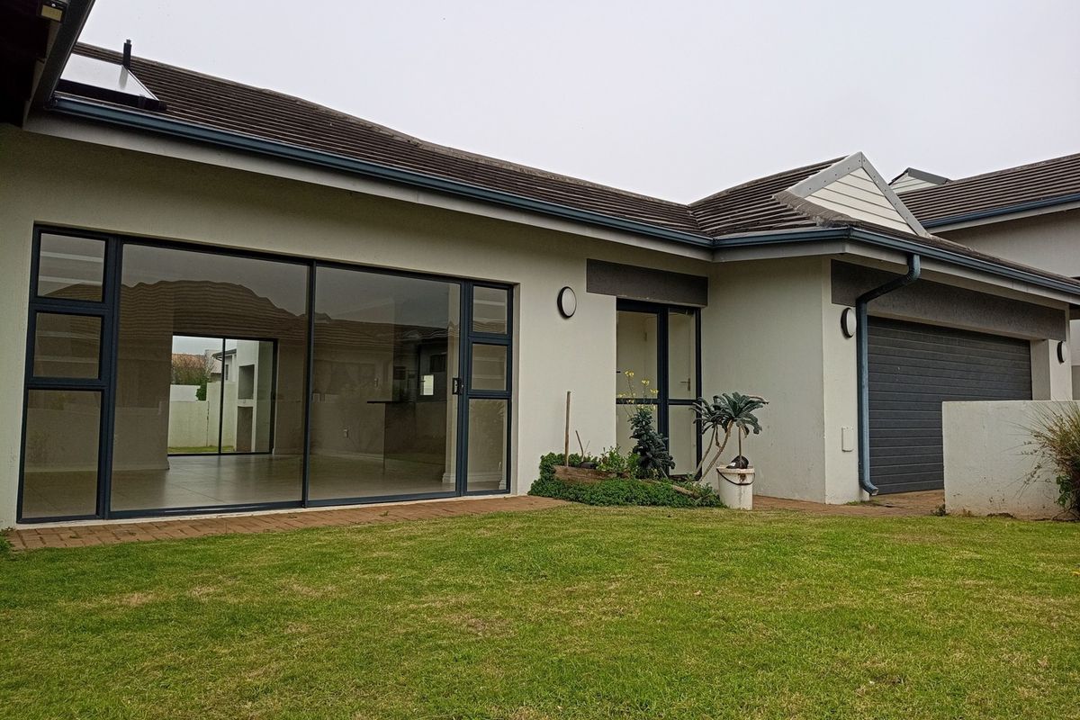 Rear view of the property featuring a paved patio area, large sliding glass doors, and an attached double garage with a well-maintained lawn.